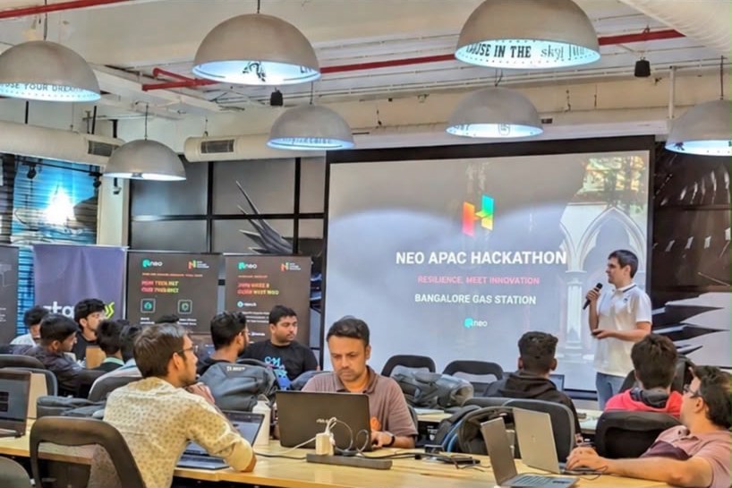 A speaker presents on stage at the Neo APAC Hackathon in Bangalore while students build at their laptops