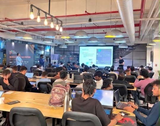 A long hall of students coding together under industrial pendant lights